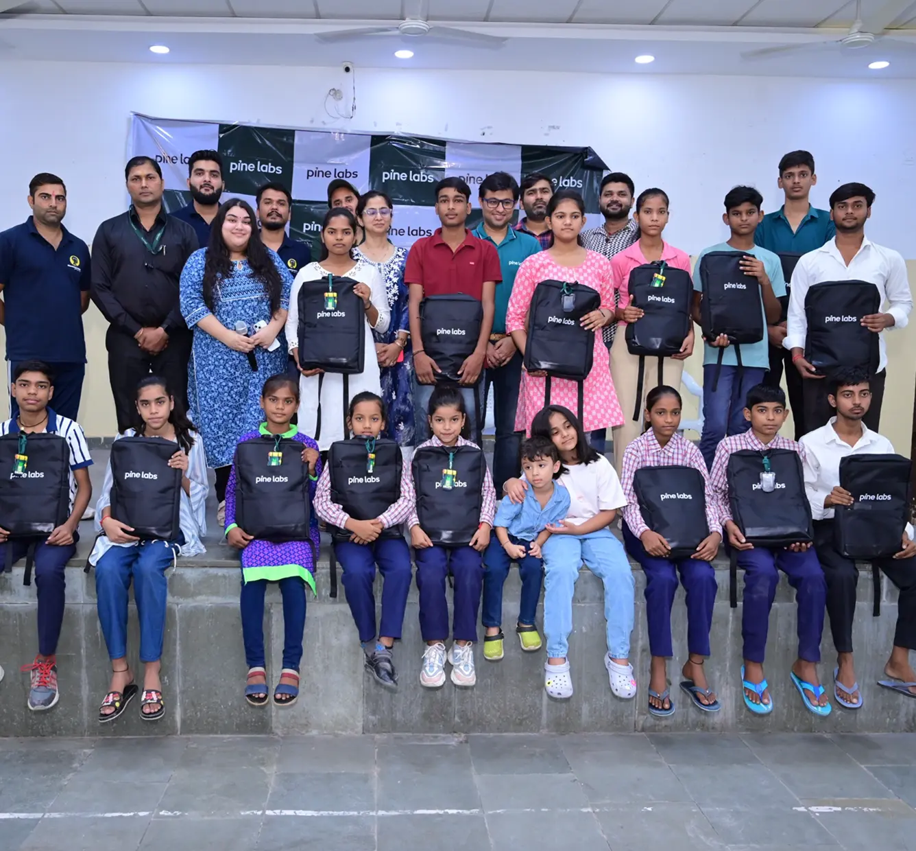 roup photo of Pine Labs volunteers with underprivileged children holding educational kits as part of a community support initiative